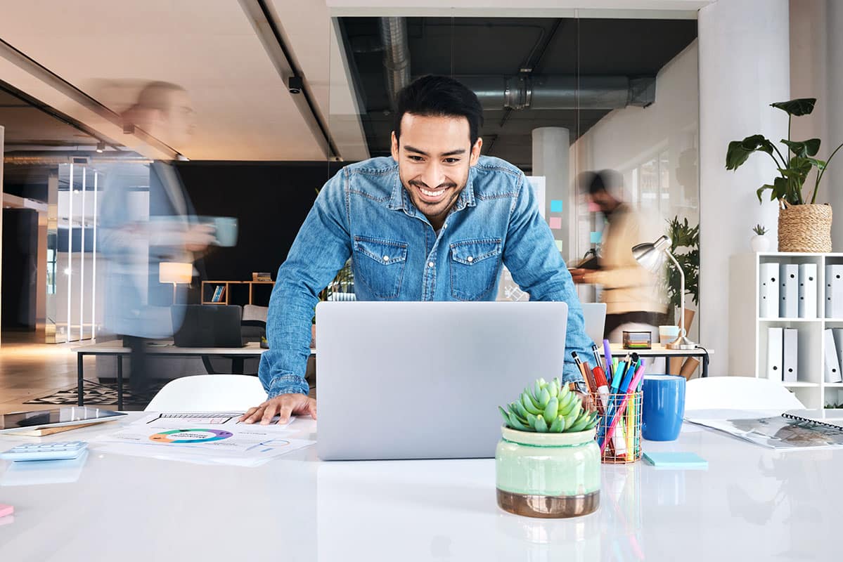 happy business man in office standing while looking at his laptop
