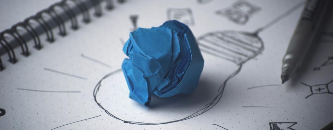 Blue paper crumbled up sitting on a paper with drawing of a lightbulb