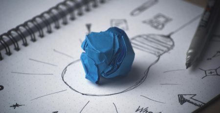 Blue paper crumbled up sitting on a paper with drawing of a lightbulb